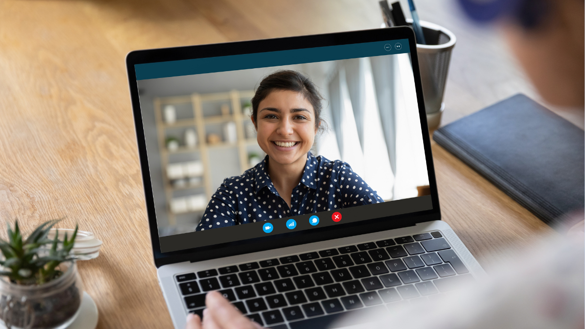 A MacBook with a lady on the screen over a video call. She's wearing a polka dot shirt and smiling