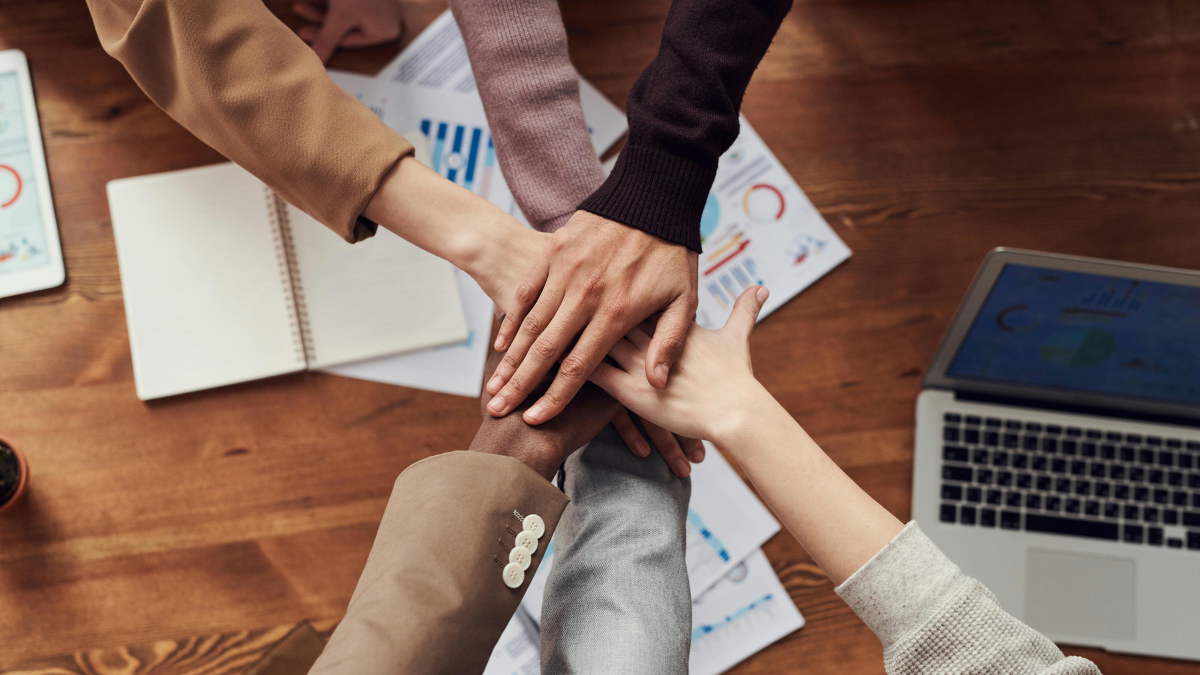 6 hands in a huddle over an office table, It's a mix of men and women